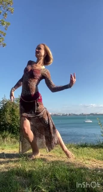 Алла танцует на траве на фоне воды и голубого неба
