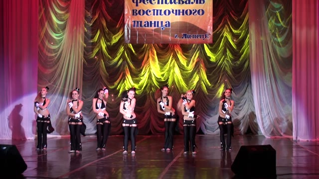 Ансамбль в чёрно-белых костюмах на сцене с красным занавесом